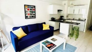 A modern living room with a blue sofa, a white coffee table, and a kitchen in the background. - Apartment with garden, reduced mobility access (Bordeaux)