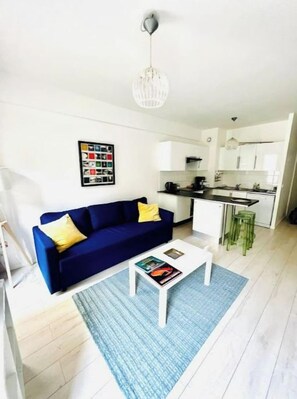 A modern living room with a blue sofa, a white coffee table, and a kitchen in the background.