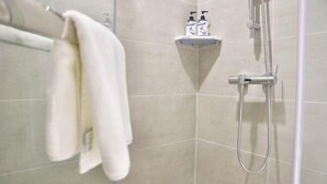 A shower with a handheld showerhead and a wall-mounted faucet. There is a towel rack with a white towel hanging on it. A shelf with two bottles of shampoo and conditioner is visible. - Homeinn · neo (Shangrao Yushan Tianjie) (Yushan)
