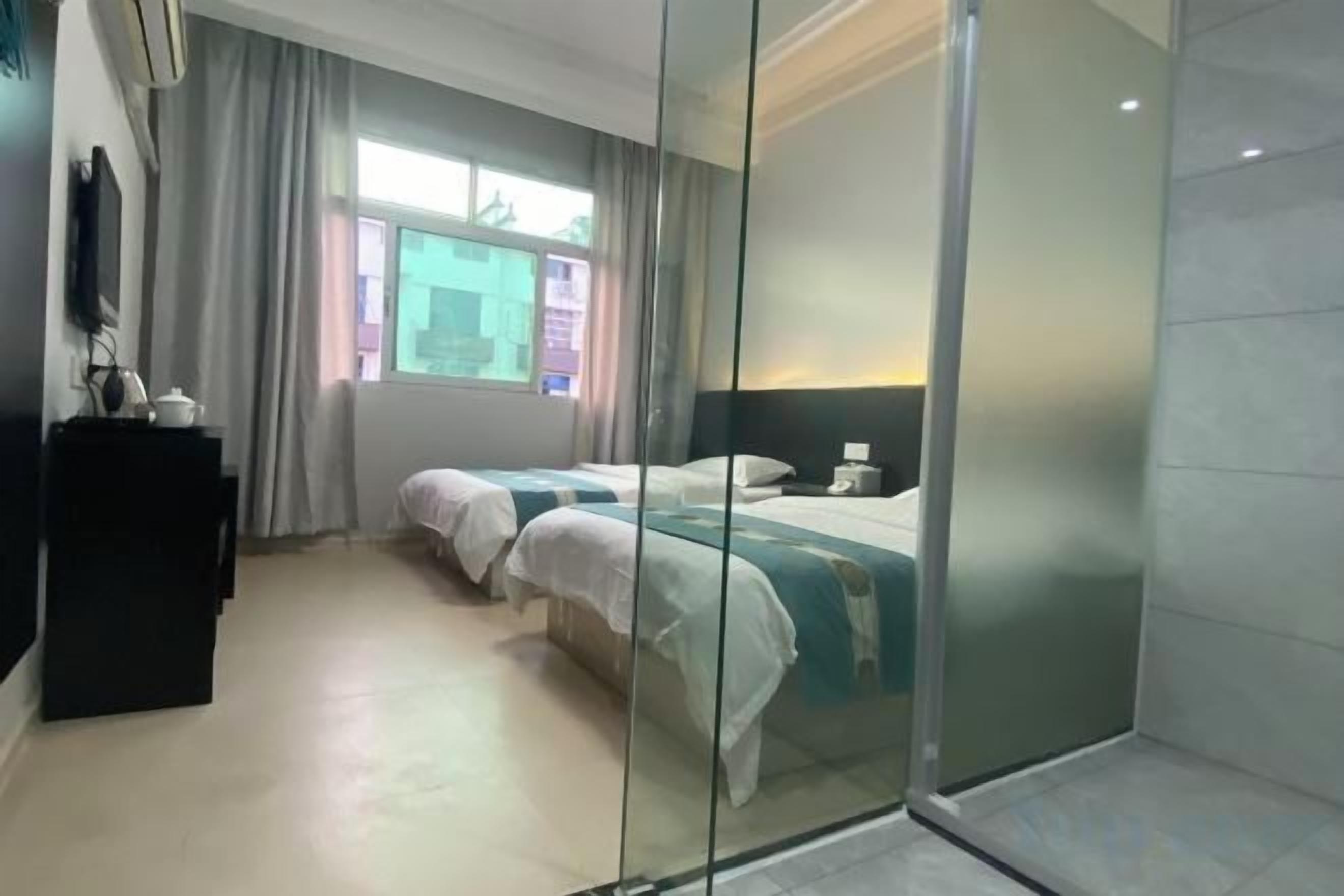 A hotel room with two beds, a desk, and a large window.