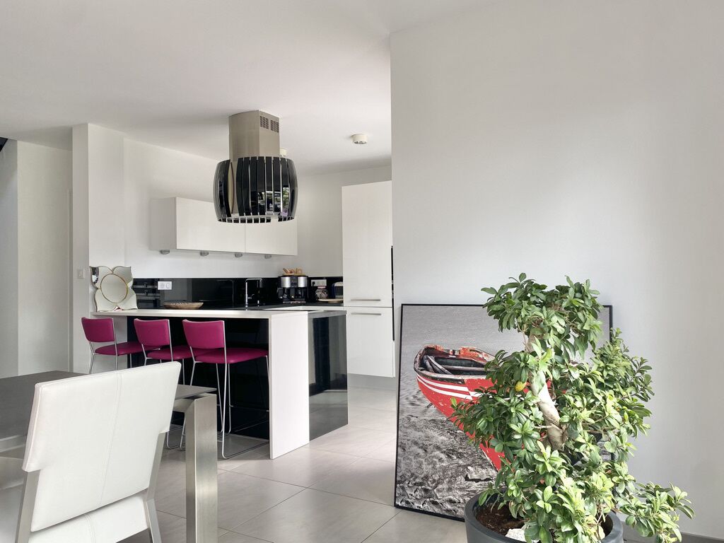 A modern kitchen with white cabinets, a stainless steel range hood, and a dining area with a white chair and a potted plant.