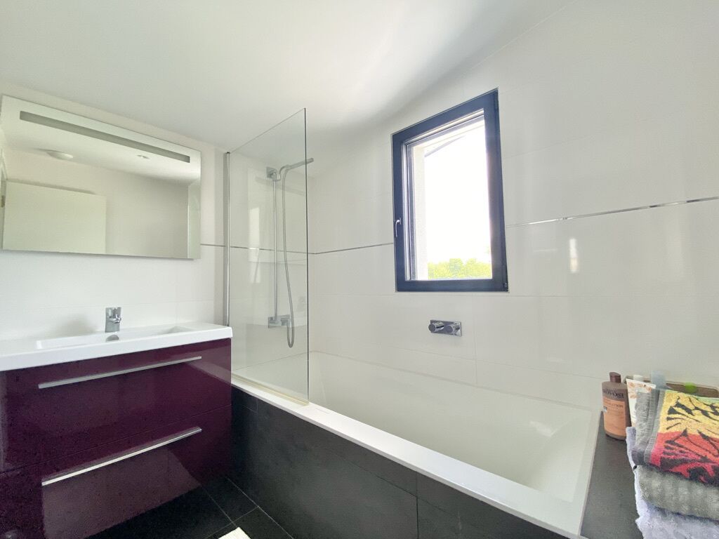 Ein modernes Badezimmer mit Duschkabine aus Glas, einem weißen Waschtisch mit Spiegel und einem kleinen Fenster.