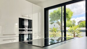 A modern kitchen with white cabinets, stainless steel appliances, and a large window offering a view of greenery. - Design Villa with Heated Pool, Garden & Beaches 5 min Away (Concarneau)