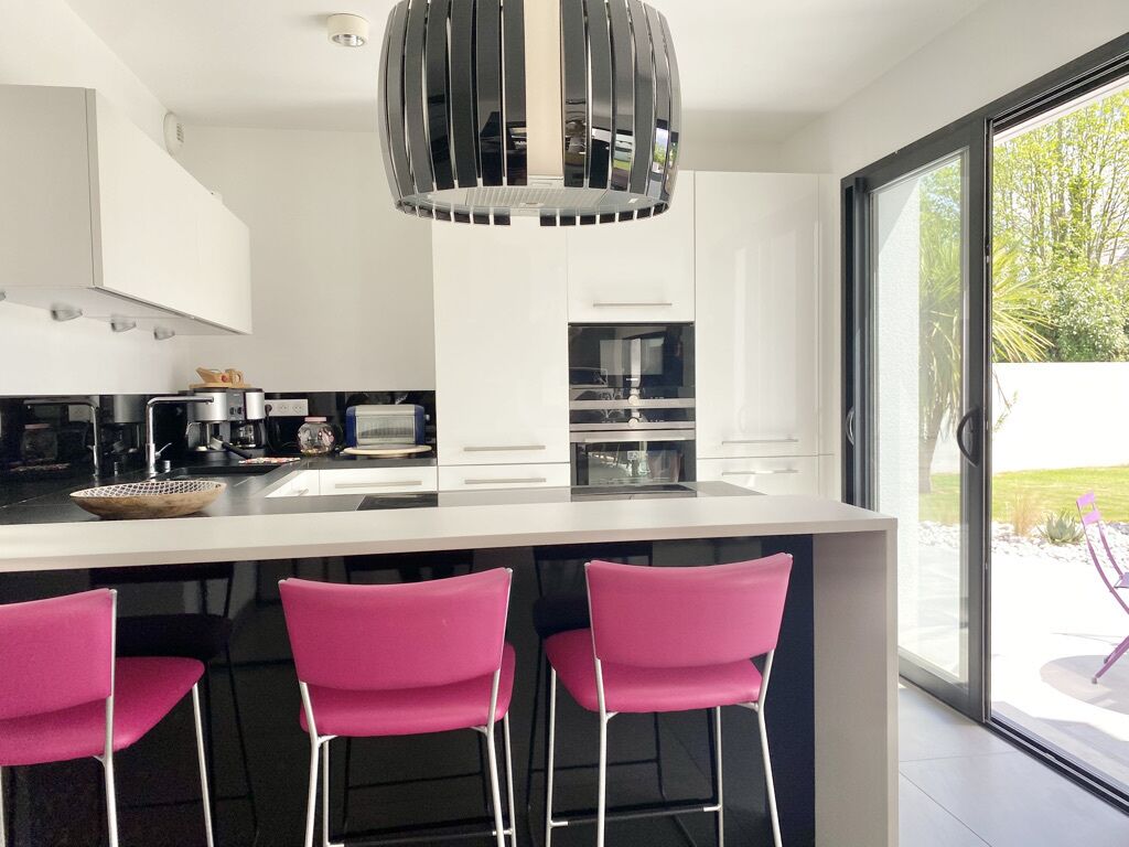 A modern kitchen with white cabinets, a central island with pink bar stools, and a large window with a view of greenery.