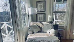 Une chambre à coucher avec un lit, une table ronde en bois, une plante en pot et un tableau encadré au mur.