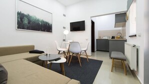 Una sala de estar moderna con un sofá, una mesa de comedor con sillas, un televisor montado en la pared y una zona de cocina con encimera y armarios.