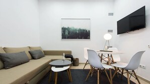 Una sala de estar moderna con un sofá, una mesita redonda y dos sillones. Un televisor de pantalla plana está montado en la pared sobre la mesa.