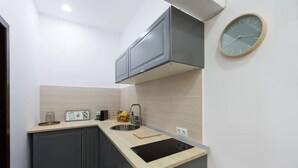 Una cocina compacta con armarios oscuros, una encimera clara, un lavamanos de acero inoxidable y un reloj de pared.