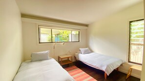 Cozy retreat with two single beds, a nightstand, and a table, offering a peaceful view of the surrounding greenery.