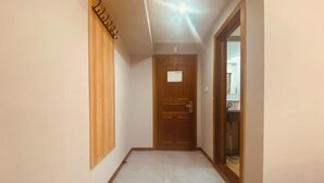 Un pasillo con una puerta de madera al final, una lámpara en el techo y un suelo de baldosas.