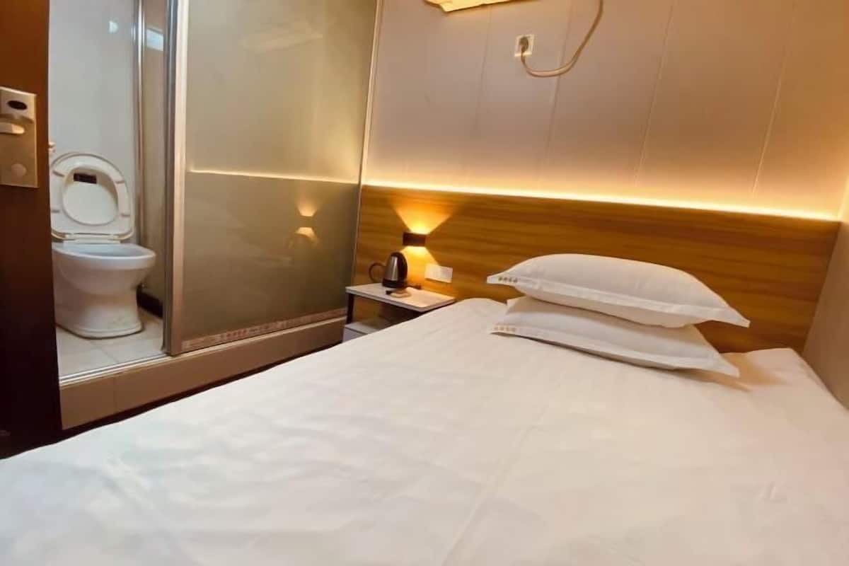 Habitación de hotel con cama, mesita de noche con lámpara, espejo y un inodoro.