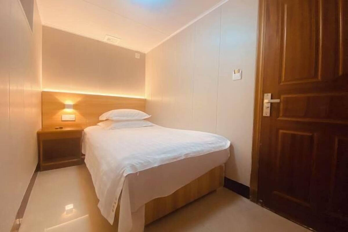 Un dormitorio pequeño y ordenado, con cama, mesita de noche y lámpara de pared.