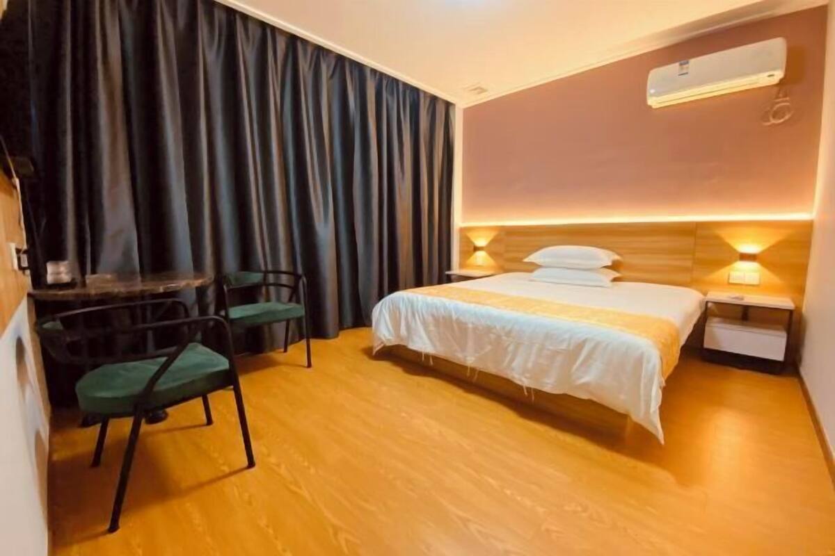 Habitación de hotel con cama, mesitas de noche, unidad de aire acondicionado, escritorio con silla y cortina.