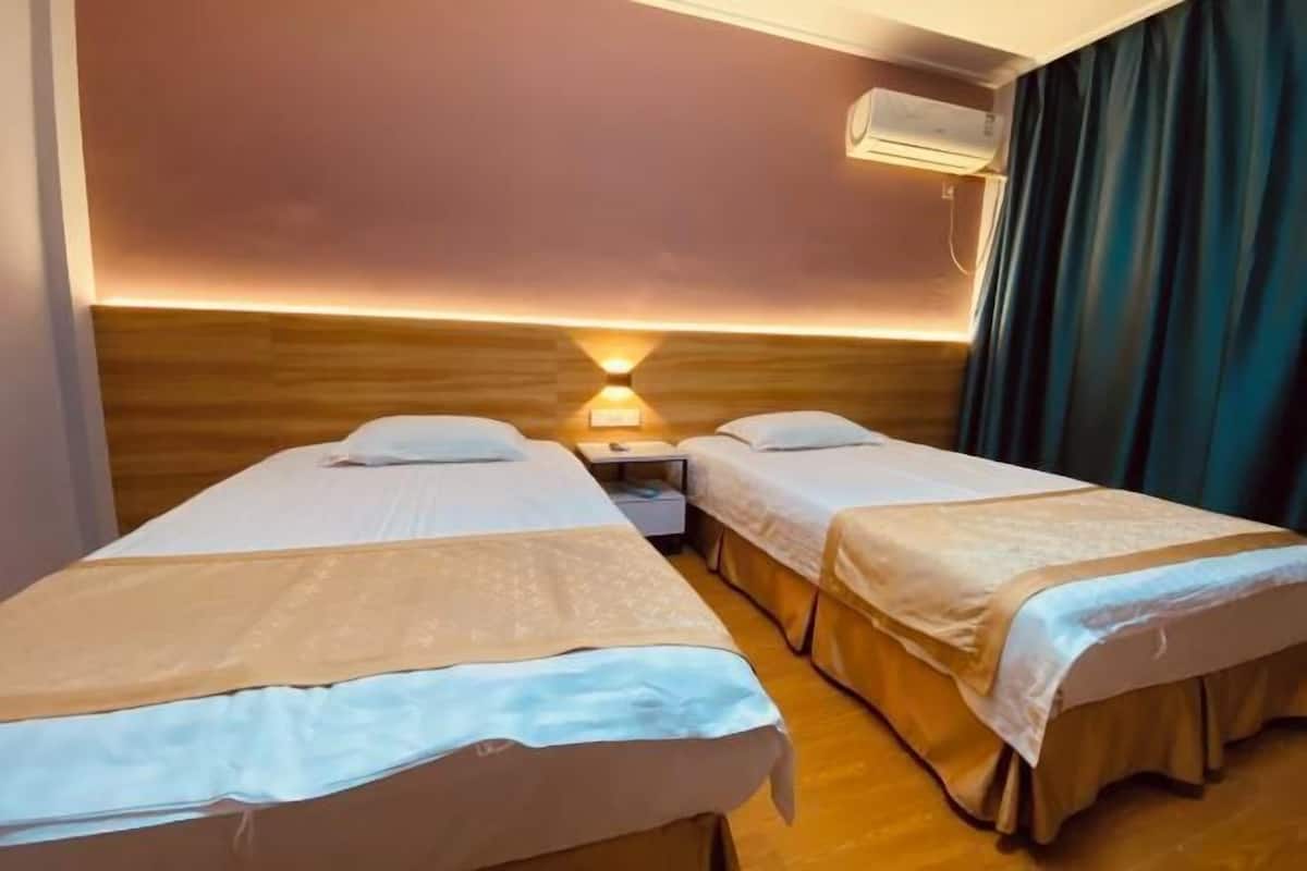 Habitación de hotel con dos camas individuales, una mesita de noche, una lámpara y un equipo de aire acondicionado.