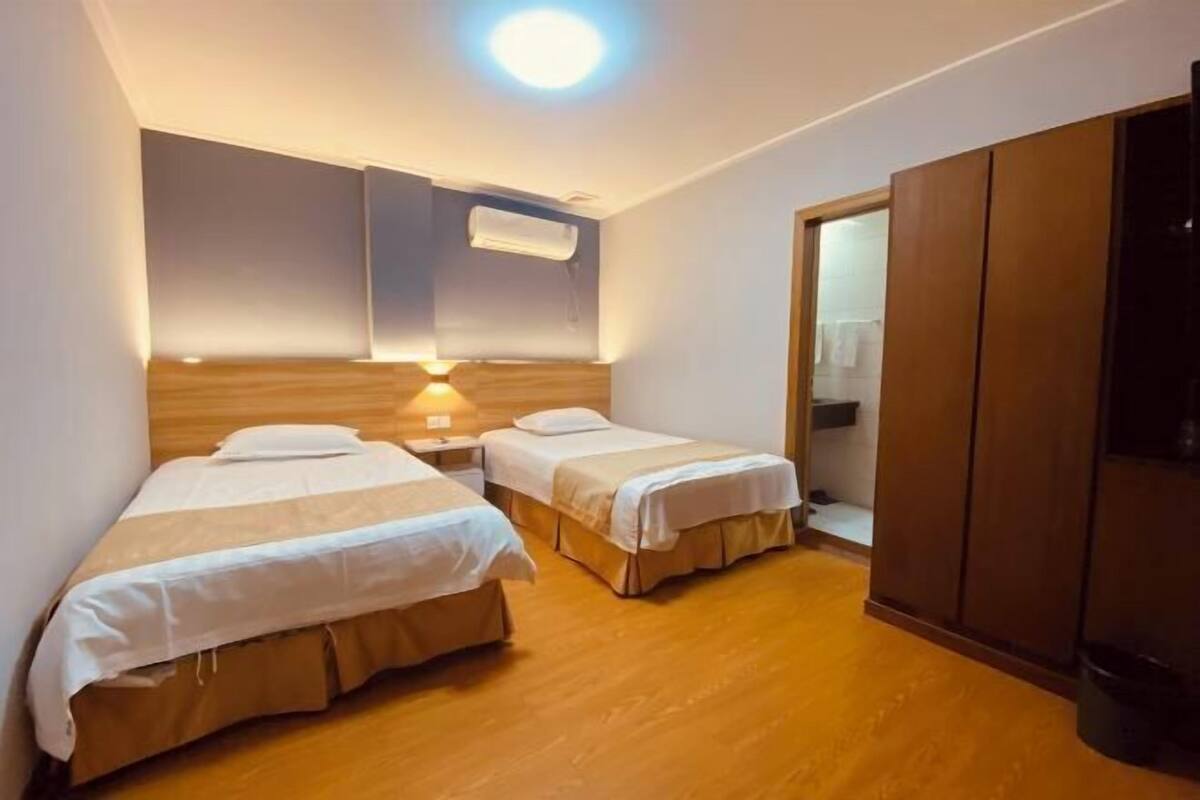 Habitación de hotel con dos camas individuales, un armario de madera, una lámpara de techo y un aire acondicionado de pared.