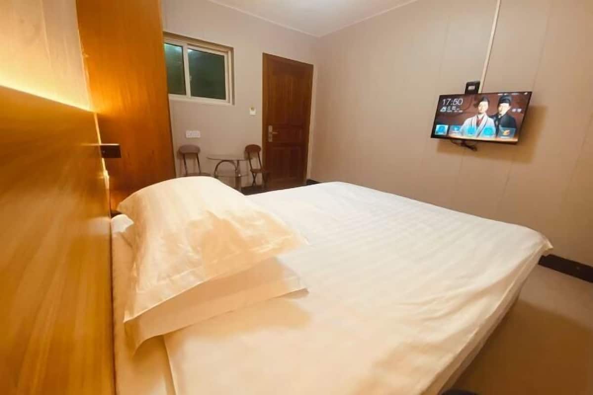 Un dormitorio con una cama, un televisor en la pared y una puerta de madera.
