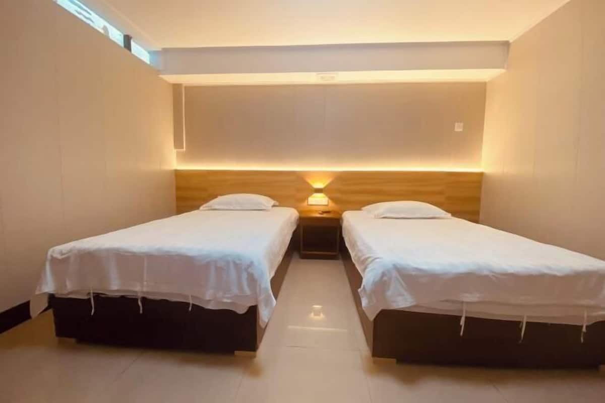 Una habitación con dos camas individuales, cabecera de madera y una lámpara fijada a la pared.
