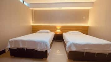 A room with two single beds, a wooden headboard, and a wall-mounted light fixture.