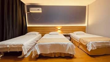 A room with three single beds, a wall-mounted air conditioner, and a bedside table with a lamp.