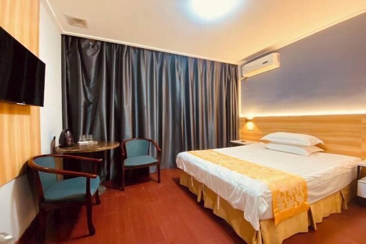 Habitación de hotel con cama, escritorio, dos sillas, televisión y ventana con cortinas.