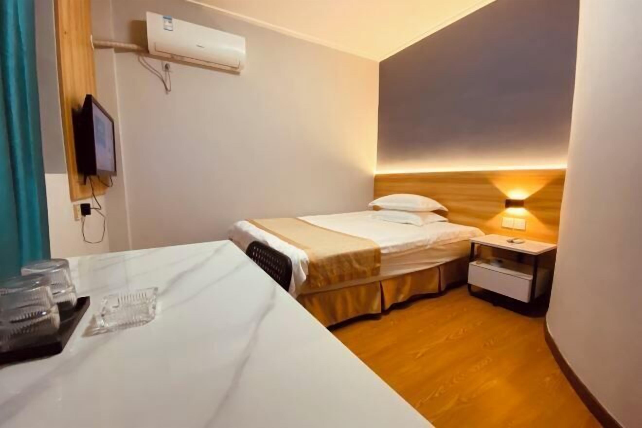 A hotel room with a bed, bedside table, and a wall-mounted air conditioner.