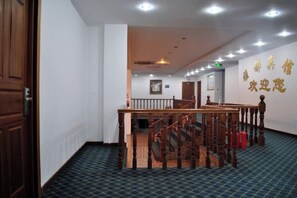 A hotel corridor with a wooden staircase, a blue carpeted floor, and a wall with golden text. - Yadu Hotel (Liyang)