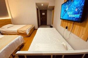 Habitación de hotel con dos camas individuales, un televisor montado en la pared y suelo de madera.