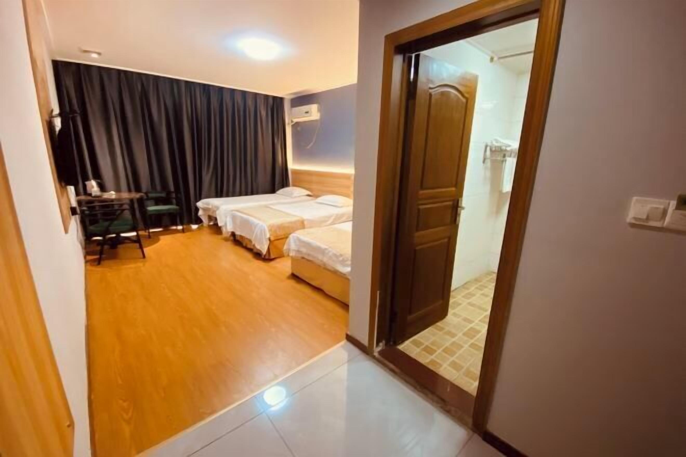 Una habitación de hotel con suelo de madera, una cama con ropa blanca, un escritorio con silla y un espejo grande.