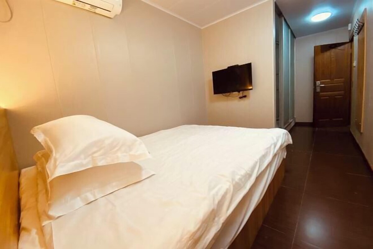 A single bed with white bedding in a room with a flat-screen TV mounted on the wall.