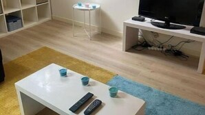 Un saló amb una taula de cafè blanca, un televisor sobre un suport, un rellotge a la paret i una taula blanca petita amb tasses.