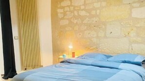 Un dormitori amb llit, una tauleta de nit amb làmpada, un radiador i una paret de pedra.