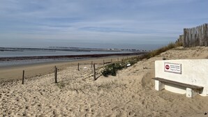 Una playa arenosa con una valla de madera y un banco.