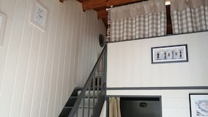 Una escalera conduce a un dormitorio tipo loft con una cortina de cuadros y un cuadro enmarcado de jarrones.
