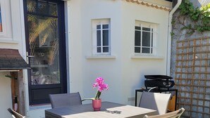 Un patio exterior con mesa y sillas, una parrilla y una planta en maceta.