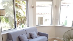 Una sala moderna con un sofá gris, una mesa de centro blanca y un sillón de mimbre.