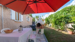 Un patio al aire libre con una mesa, sillas y un paraguas rojo.