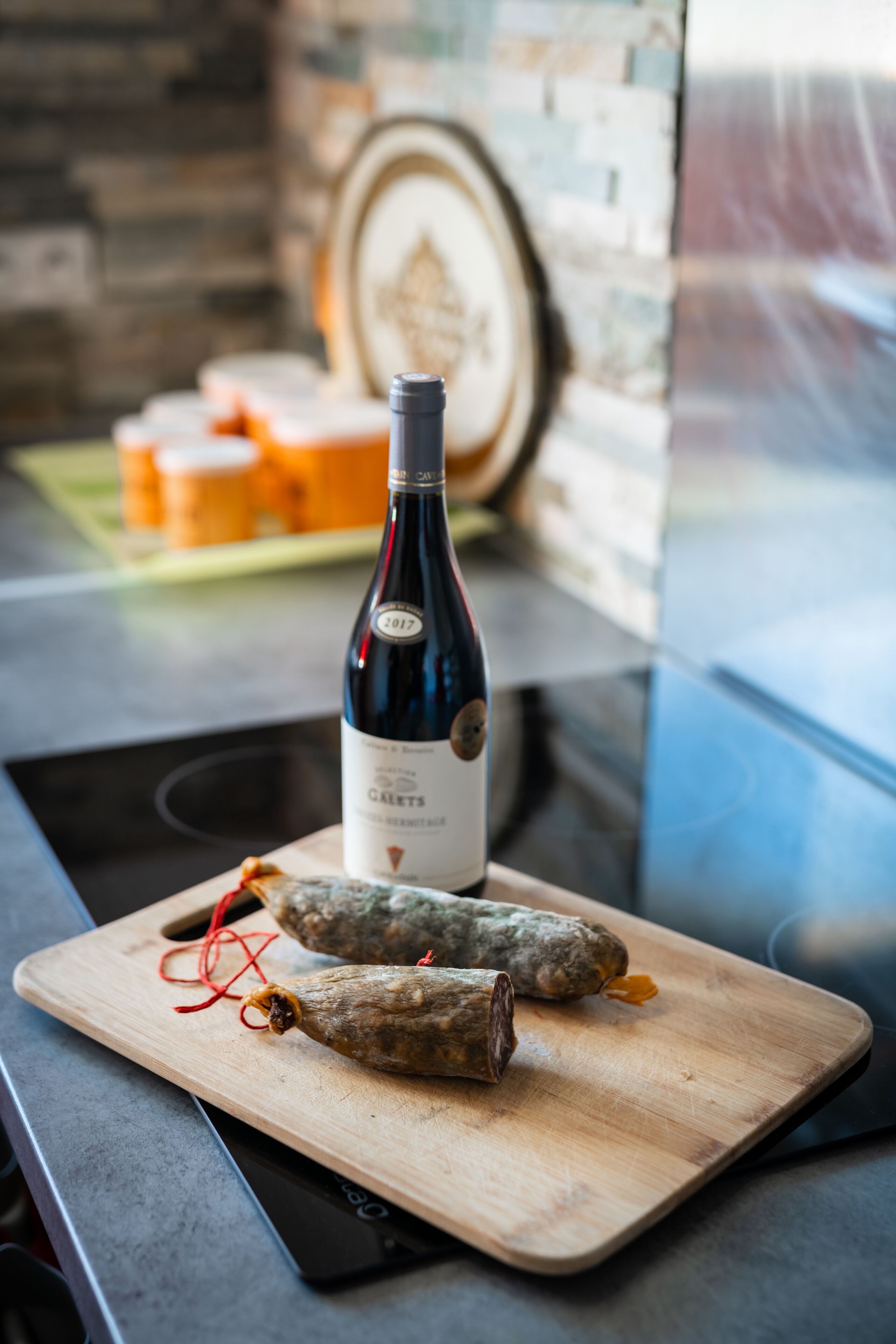 A bottle of wine on a wooden board with two cured meats.