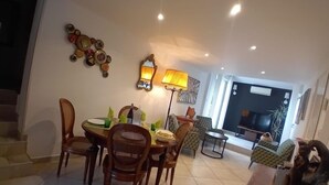 Un comedor con una mesa dispuesta para cuatro personas, rodeada de sillas de mimbre. Hay dos lámparas de pared y una pieza decorativa sobre la mesa.