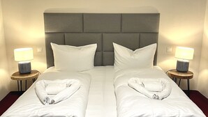 Uma cama de casal com duas almofadas, cabeceira e duas mesas de cabeceira com abajures.