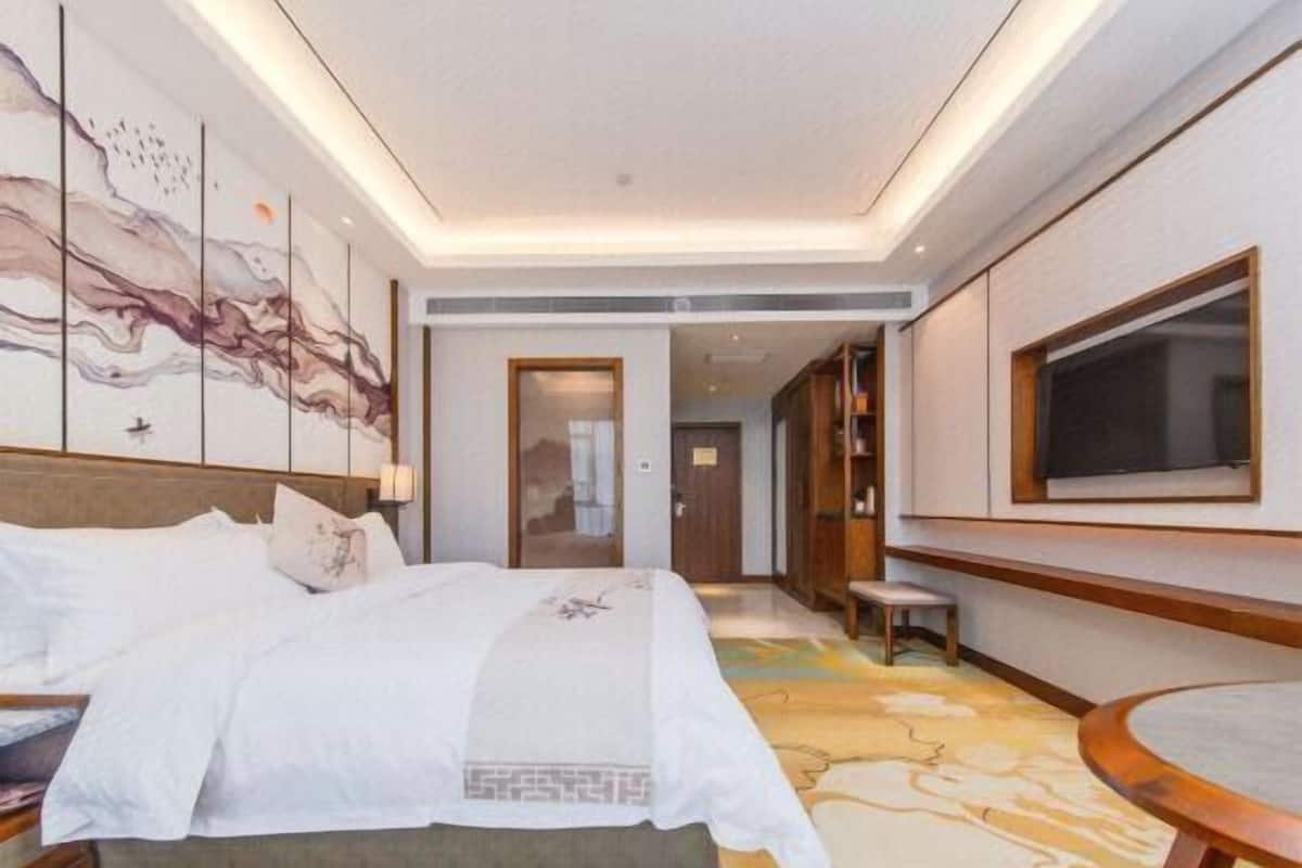 A hotel room with a large bed, a small table, a TV, and a painting on the wall.