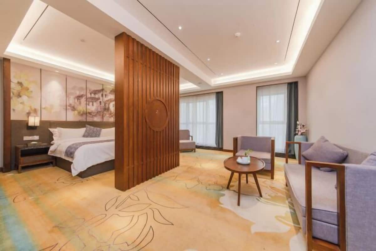 A modern hotel room with a large bed, a seating area with a round table, and a decorative wall panel.