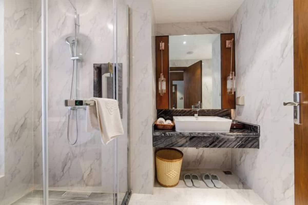 A modern bathroom with a glass-enclosed shower, a marble-tiled floor, a white sink, and a wooden vanity.