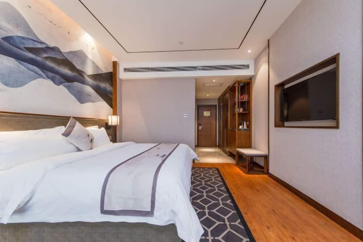 A modern hotel room with a large bed, a TV mounted on the wall, and a view of the hallway.