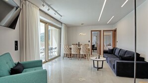 Un salon moderne comprenant un canapé, un fauteuil vert, un coin repas avec une table et des chaises, ainsi qu’une grande porte-fenêtre coulissante donnant sur une terrasse extérieure.