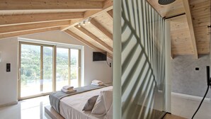 Une chambre avec une grande fenêtre, des poutres apparentes en bois au plafond, un lit avec des oreillers et un espace douche.