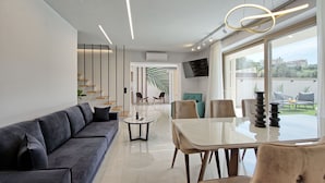 Un espace repas moderne avec une table et des chaises en verre, un canapé et un escalier agrémenté d’une plante.