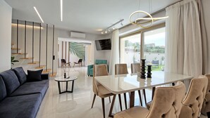 Un salon moderne avec une table à manger en verre, des sièges confortables, un téléviseur et une vue sur l’extérieur.