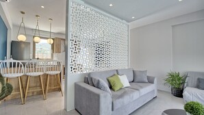 A modern living room with a grey sofa, a white partition, and a dining area with a table and chairs.