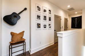 A hallway with a black guitar, a brown cushion on a stool, and a series of black-and-white photographs on the wall.