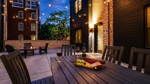 An outdoor patio with wooden furniture, a table set with a bottle of wine, glasses, and a fruit platter. - Nashville Escape • Whiskey & Western Vibes (Nashville)